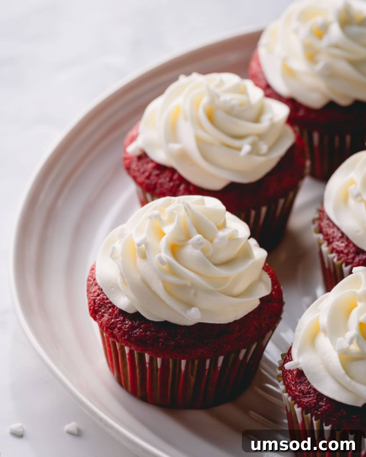A close-up view of several red velvet cupcakes arranged on a white platter, each topped with a generous swirl of cream cheese frosting.