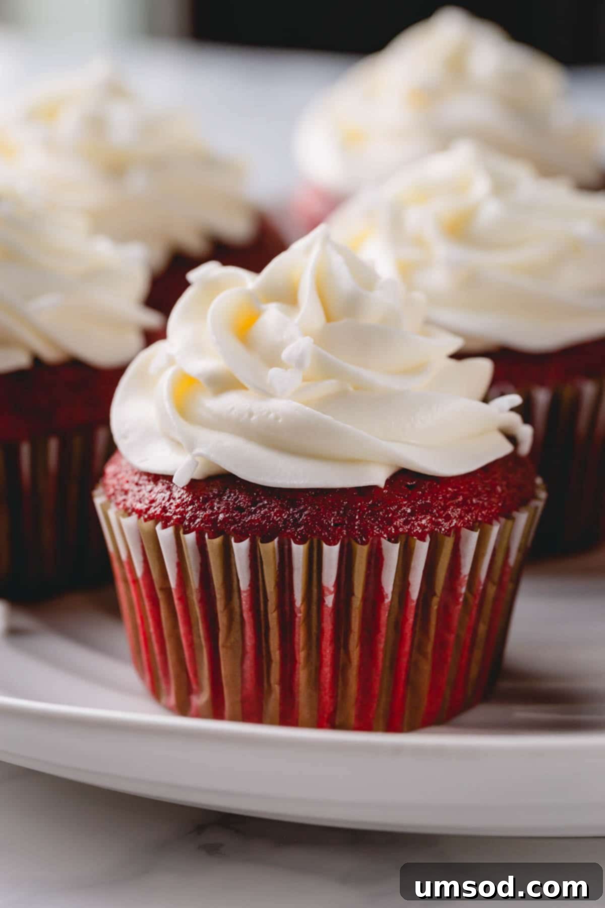 A single red velvet cupcake with luscious cream cheese frosting, garnished with red sprinkles, presented on a minimalist white background.