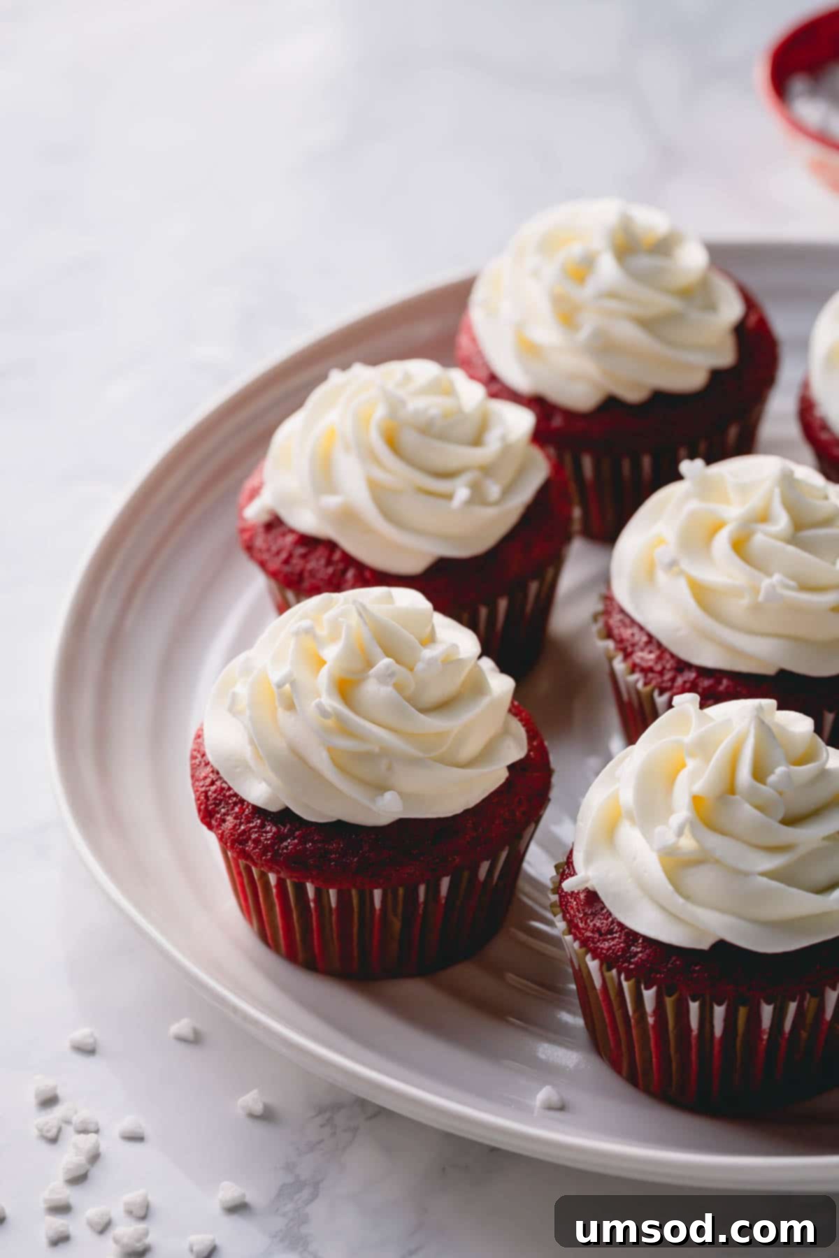 A full platter showcasing numerous red velvet cupcakes, each meticulously frosted with a high swirl of cream cheese frosting.