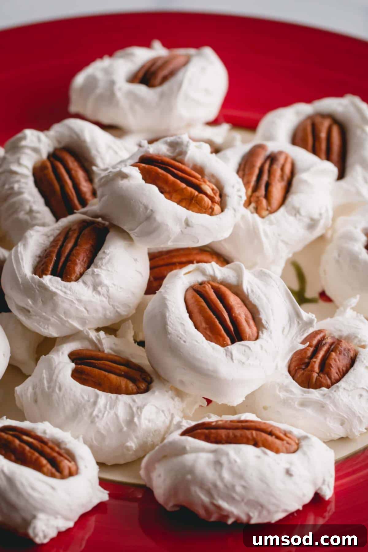 A generous pile of pristine white divinity candies, each topped with a delicate pecan half, arranged on a vibrant red plate.
