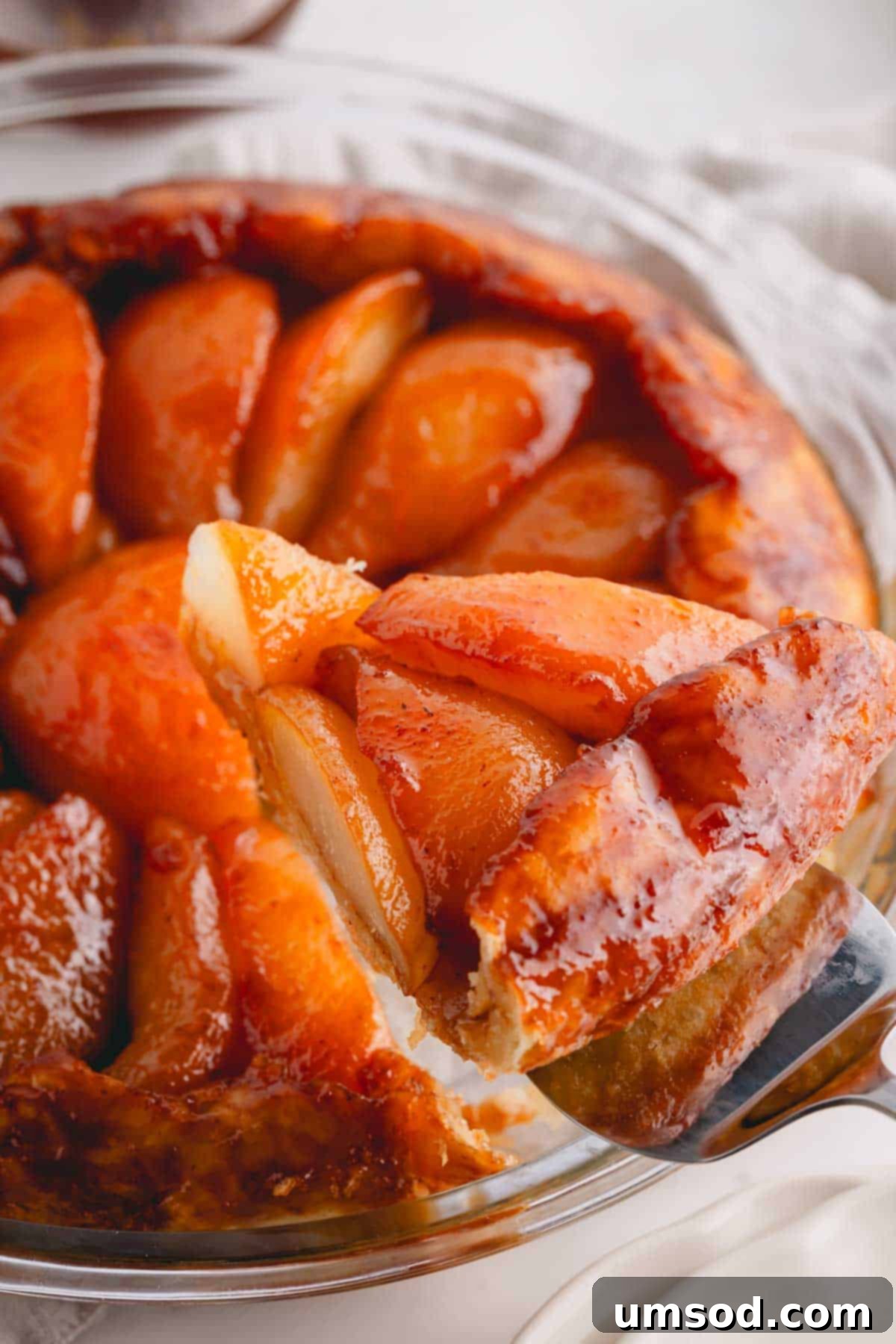 Golden Caramel Pear Tart 3 A slice of pear tarte tatin being lifted from a glass pie dish, showing the beautiful caramelized pears.