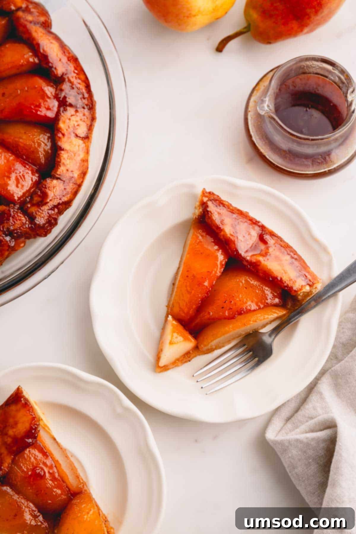 Golden Caramel Pear Tart 4 A slice of pear tarte tatin on a white plate with a fork, ready to be enjoyed.