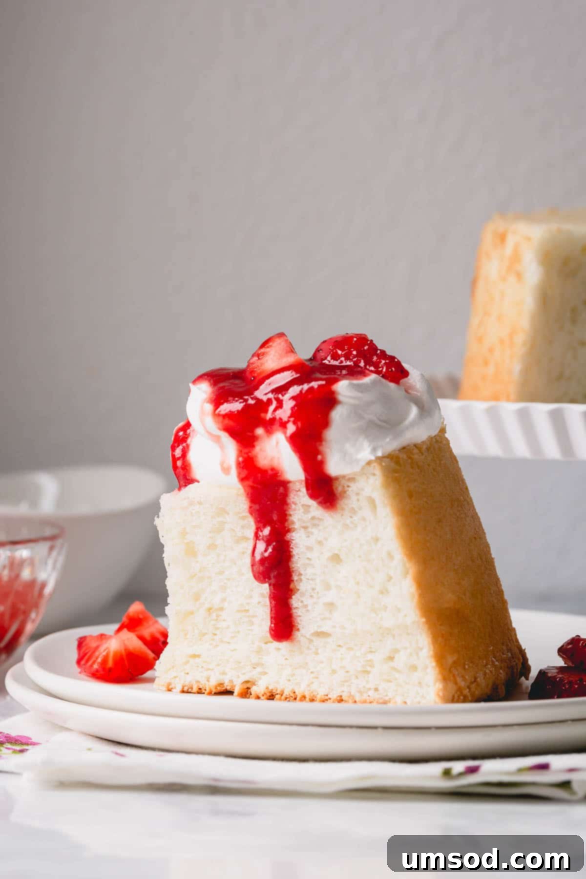 Cloud Nine Angel Food Cake 2 A slice of angel food cake topped with whipped cream and strawberry sauce, showcasing its light texture.
