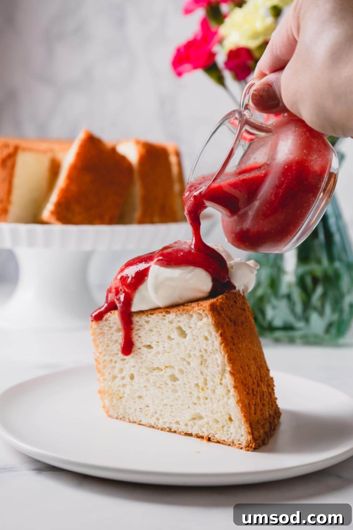 Cloud Nine Angel Food Cake 10 A slice of angel food cake topped with whipped cream and strawberry sauce, ready to be enjoyed.