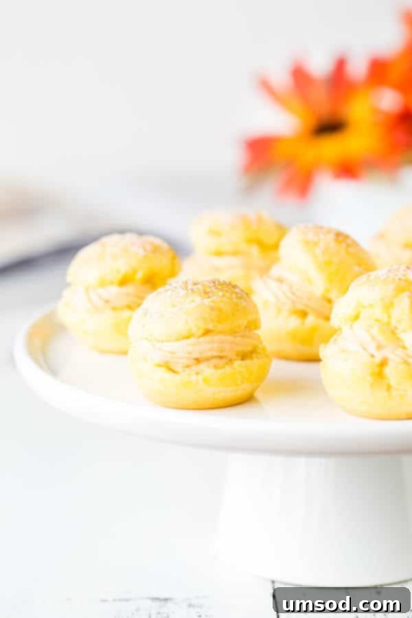A stunning stack of pumpkin cream puffs, dusted with powdered sugar, ready to be enjoyed as a festive and delicious fall treat.