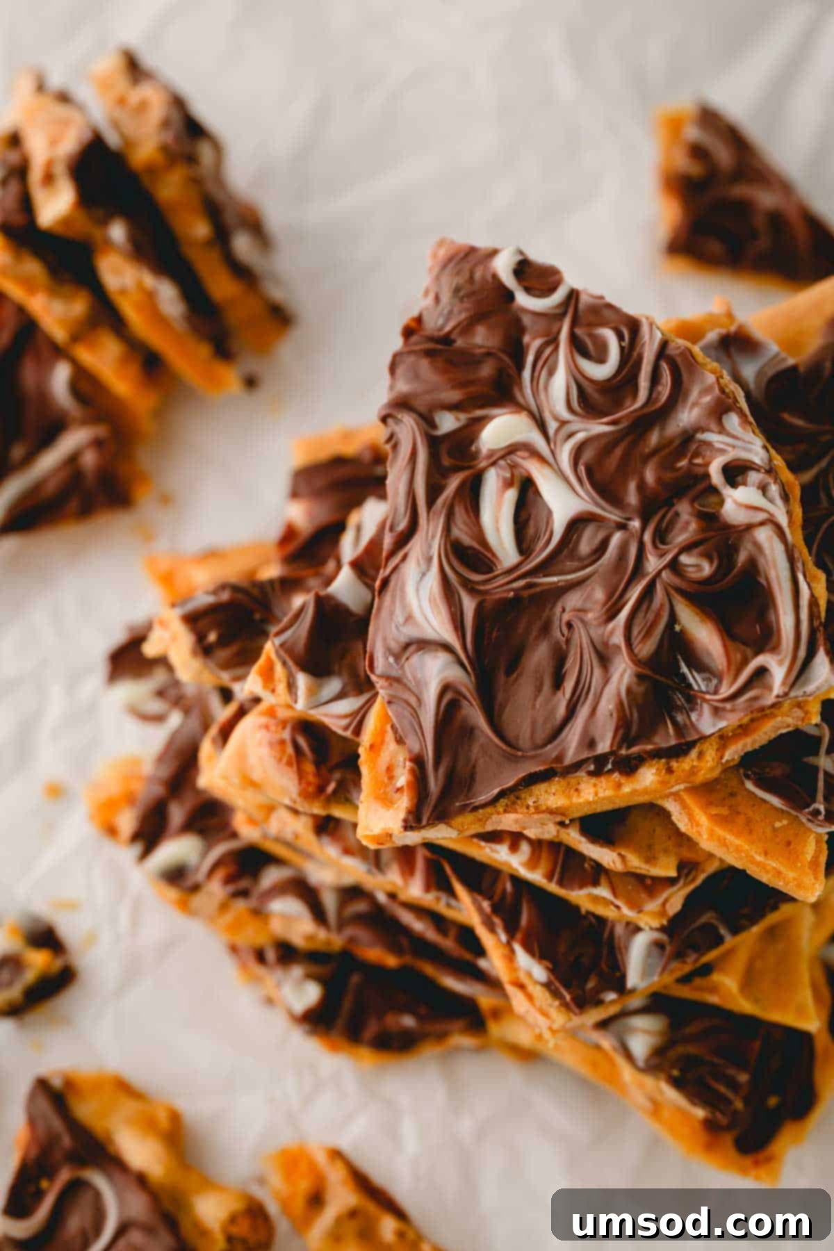 Overhead shot of chocolate peanut brittle pieces adorned with elegant white chocolate swirls, on a rustic surface.