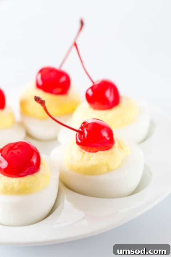 A serving platter adorned with sweet deviled eggs, some topped with a vibrant maraschino cherry, making a delightful and deceptive dessert.