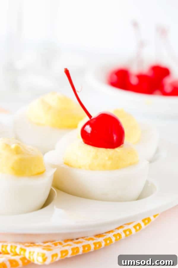 Sweet deviled eggs, one topped with a maraschino cherry, elegantly arranged on a white serving platter.