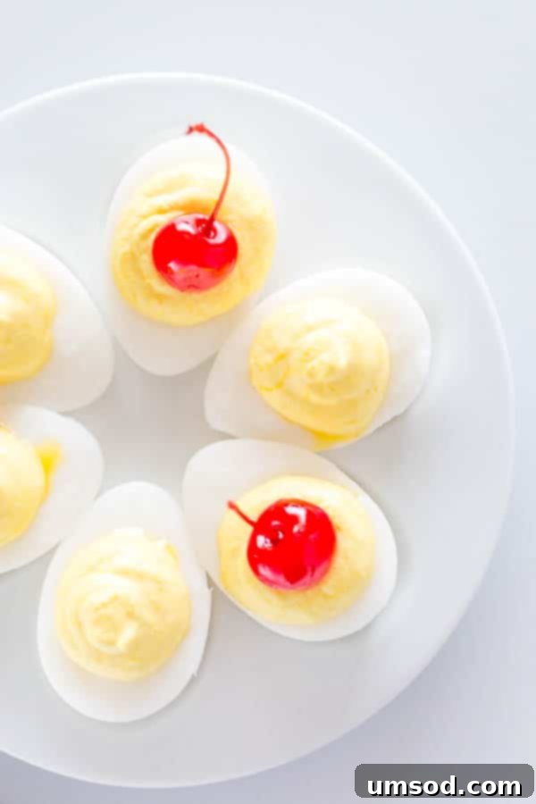 An array of sweet deviled eggs on a white serving platter, some adorned with bright red maraschino cherries.