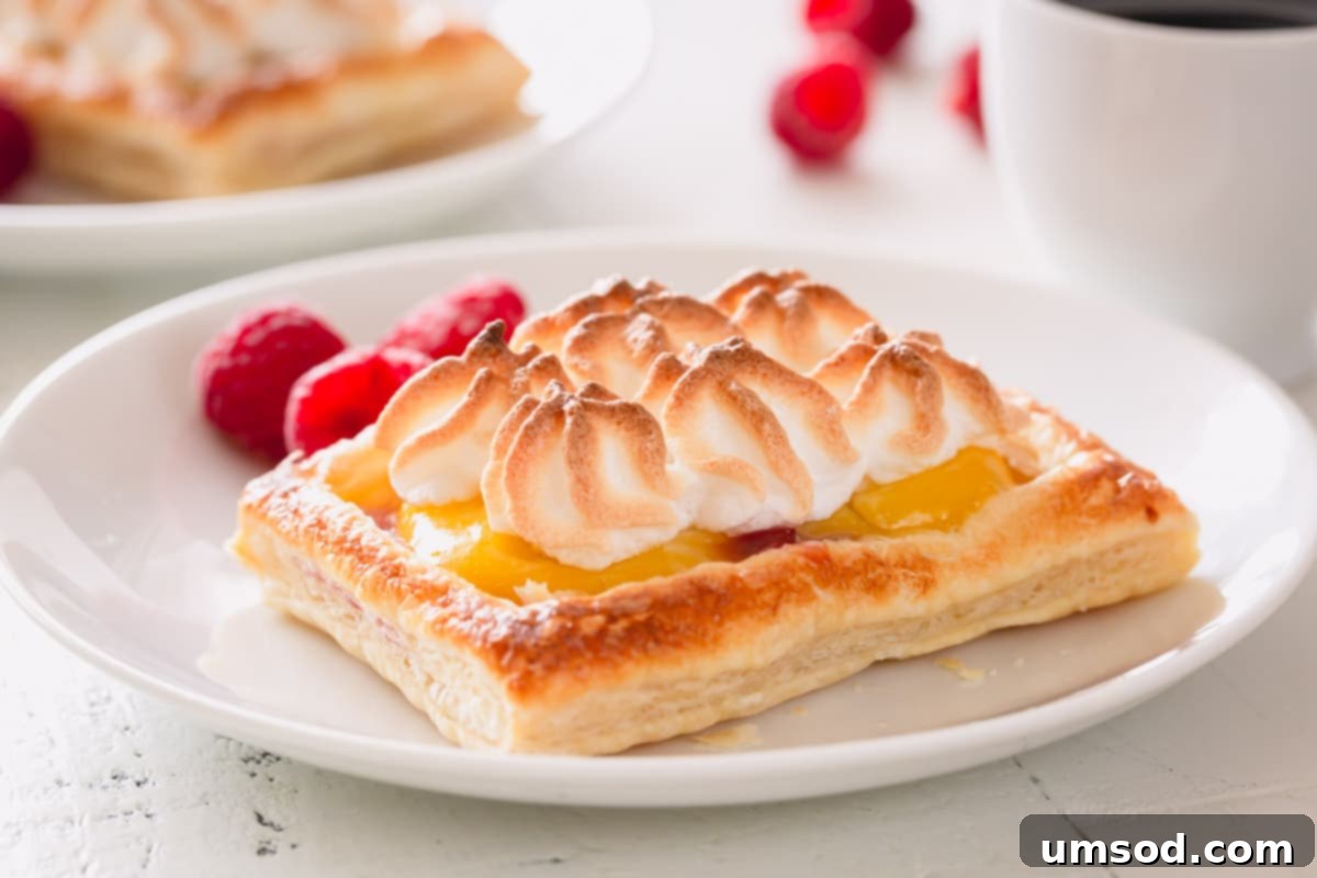 Individual raspberry lemon meringue tartlets on a white serving plate.