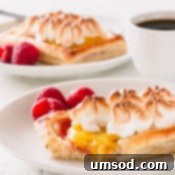 A raspberry lemon meringue tartlet on a white plate with a bite cut of off.
