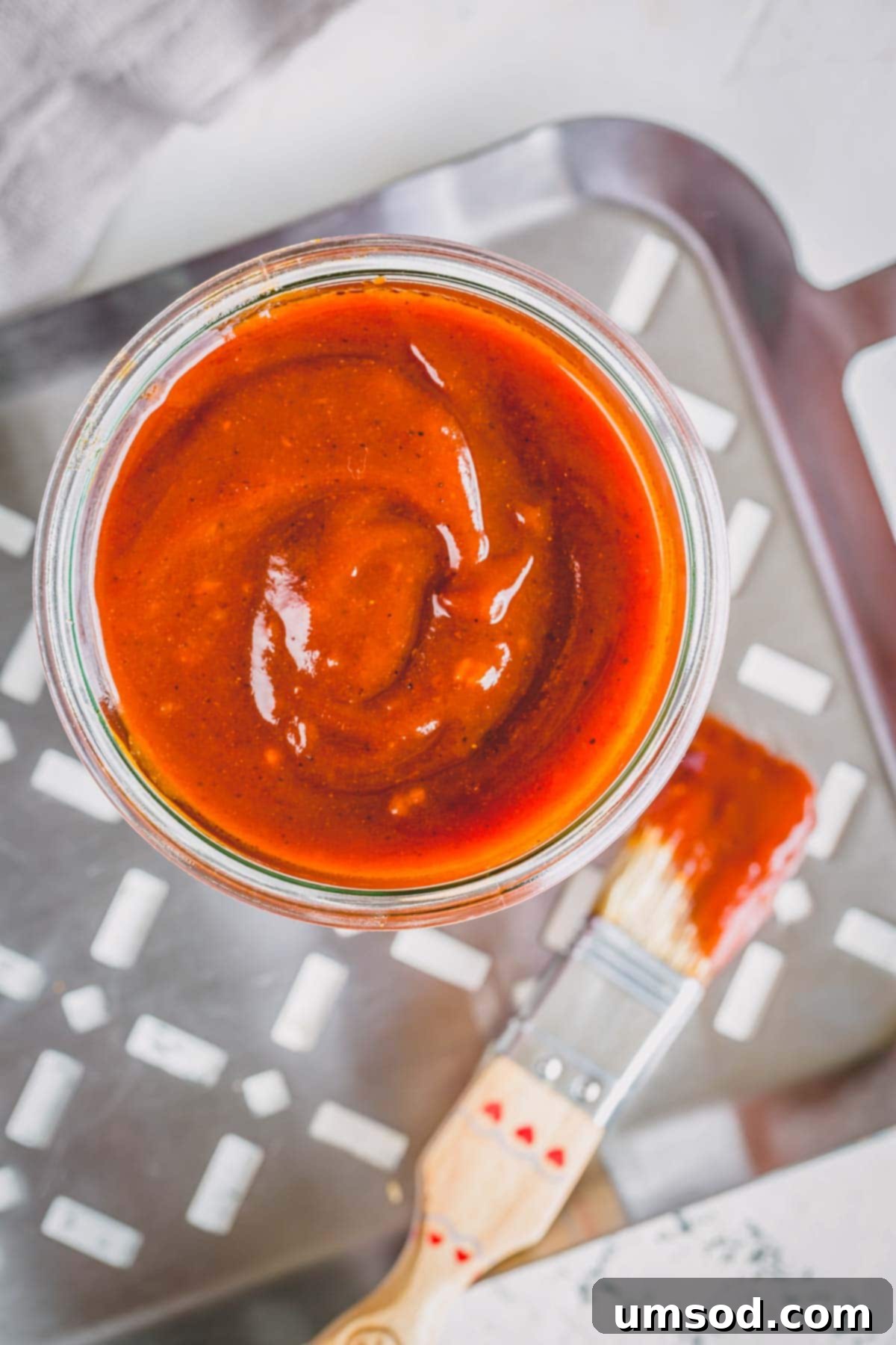 Easy Homemade BBQ Sauce Recipe 4 A jar of homemade BBQ sauce sitting on a metal grill tray, with a basting brush resting beside it, indicating readiness for use.