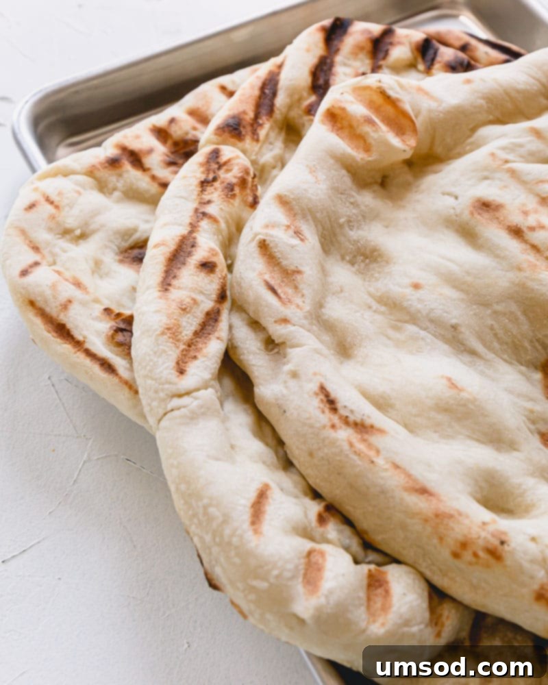 Several pre-grilled pizza crusts stacked on top of each other on a baking sheet, ready for freezing or storage.