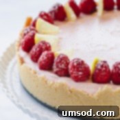 A whole lemon raspberry cheesecake topped with fresh raspberries on a white serving platter.