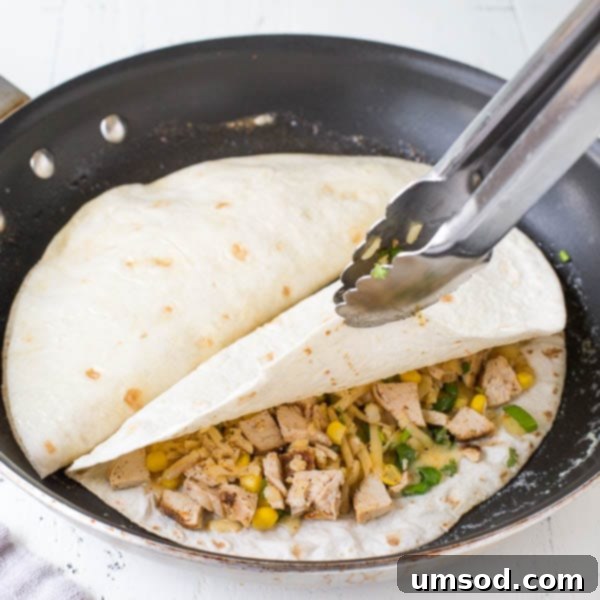 Effortless 30-Minute Cheesy Chicken Quesadillas 6 Cooking chicken quesadillas in a non-stick skillet with melted butter, pressing down with a flat spatula for a golden-brown, crispy finish.