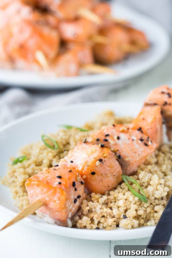 Sticky Honey Sesame Salmon Skewers 4 Close-up of golden brown honey sesame salmon kebabs on a plate with fresh herbs.