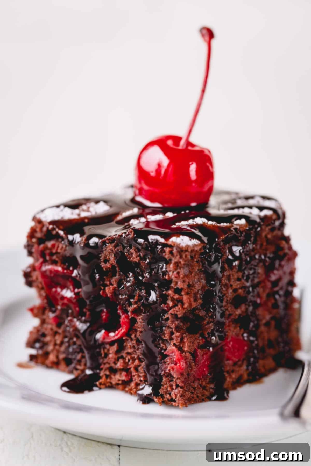 A delectable slice of 3-ingredient chocolate cherry cake, elegantly topped with a rich chocolate fudge drizzle and a vibrant maraschino cherry.