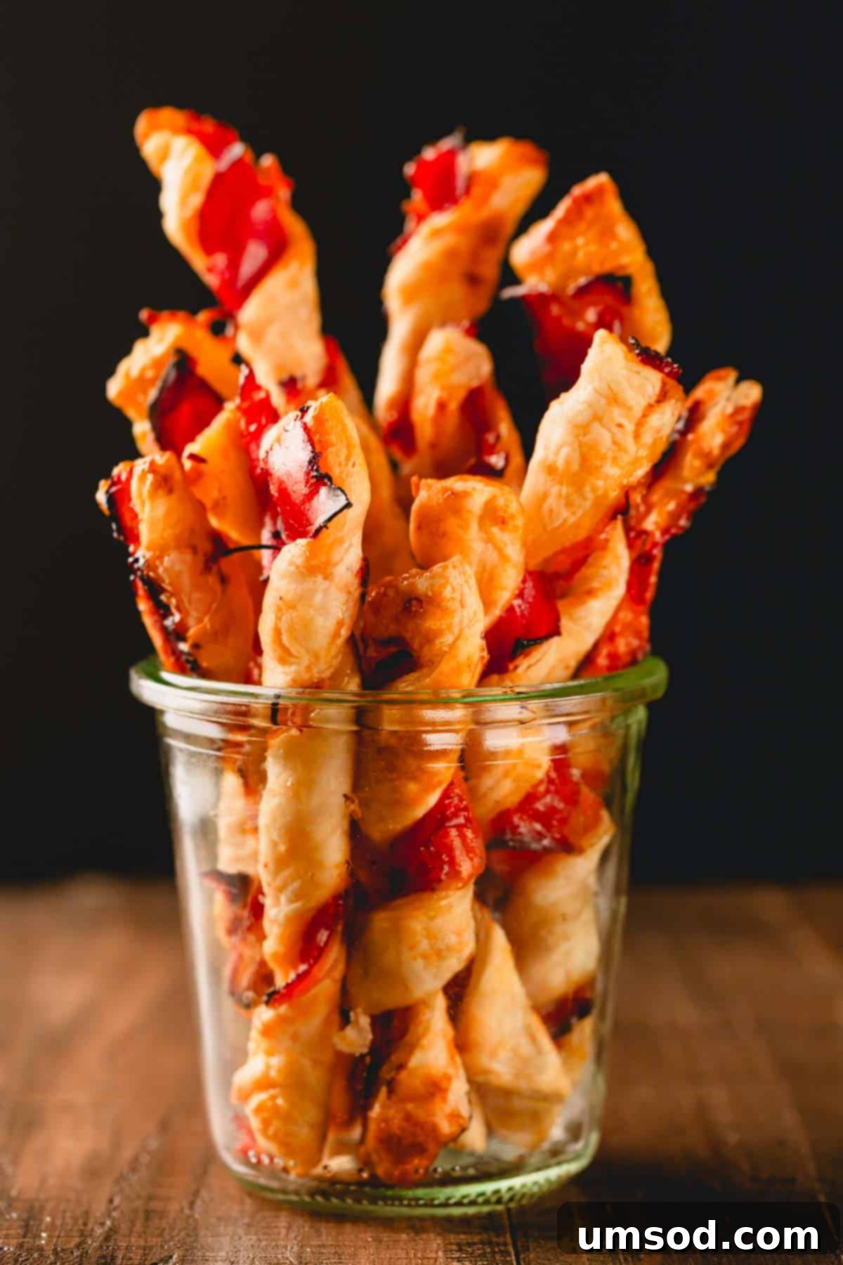 A glass jar full of baked puff pastry twists with prosciutto, perfect for storage or gifting.