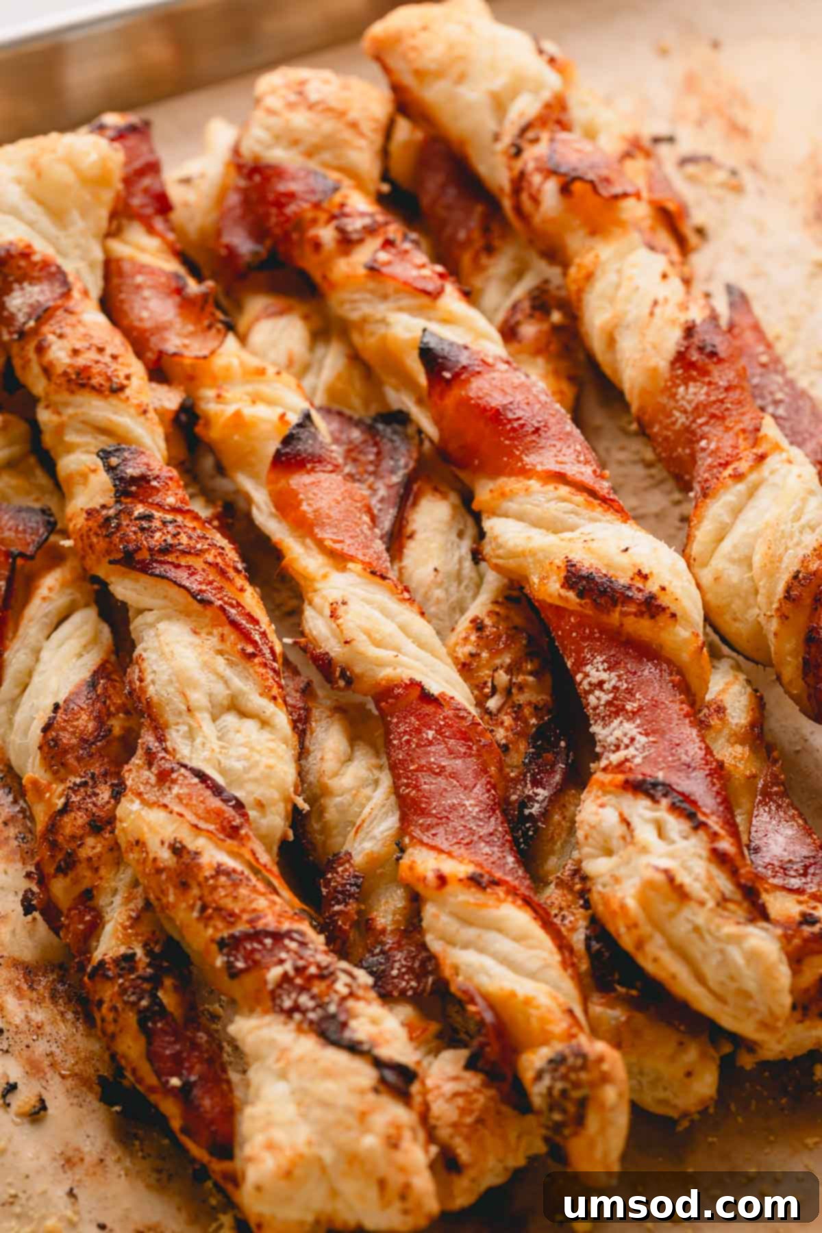 Savory puff pastry twists with prosciutto and jam on a parchment paper lined baking sheet, ready for the oven.