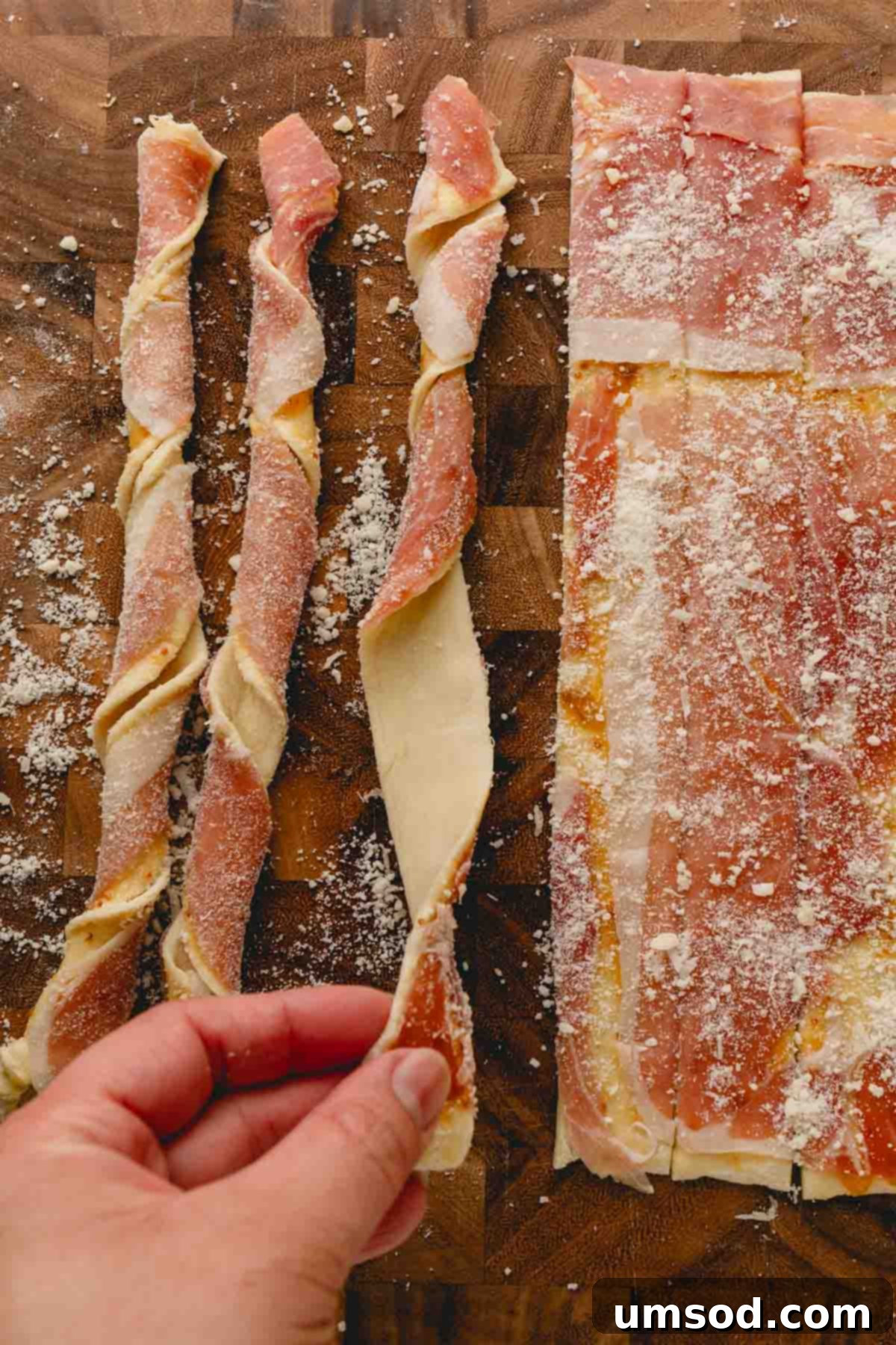 Twisting the puff pastry strips with prosciutto side out, showcasing one method.