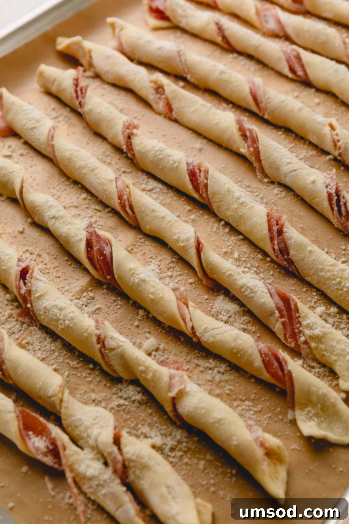Twisted the puff pastry strips with prosciutto side on the inside arranged on a baking sheet, showing an alternative method.