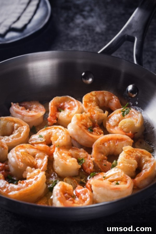 Garlic Butter Shrimp 4 Garlic butter shrimp cooking in a pan, showing the transformation from translucent to opaque and pink, with garlic sizzling in the butter.
