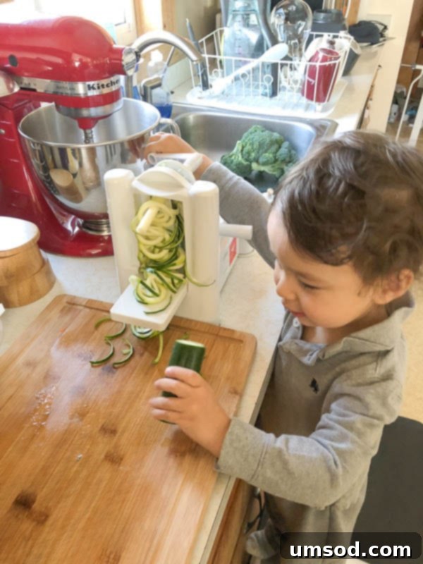 Toddler Grant helping with a spiralizer to prepare zucchini, showing his kitchen involvement.