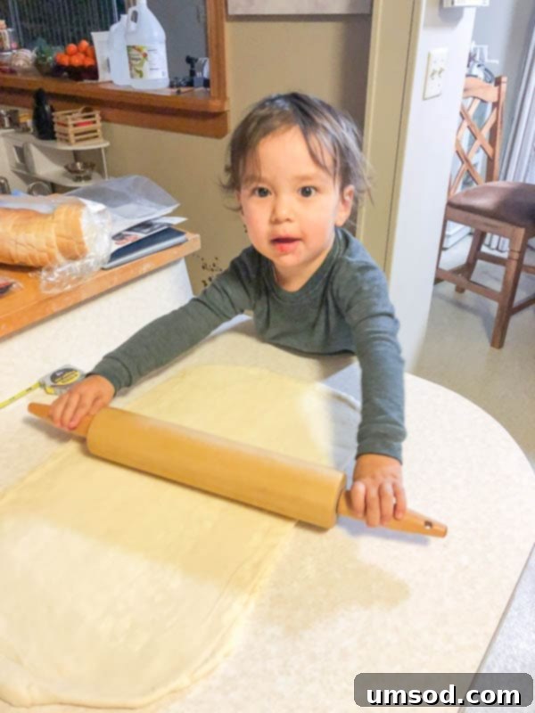 Toddler Grant rolling out dough with a small rolling pin, helping to make pain au chocolat.