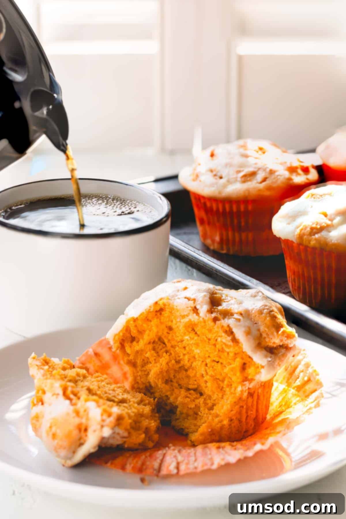 Spiced Pumpkin Cream Cheese Swirl Muffins 3 A pumpkin muffin teared in half on a plate, and coffee being poured into a mug. The inside of the muffin shows the pumpkin batter and the cream cheese swirl.