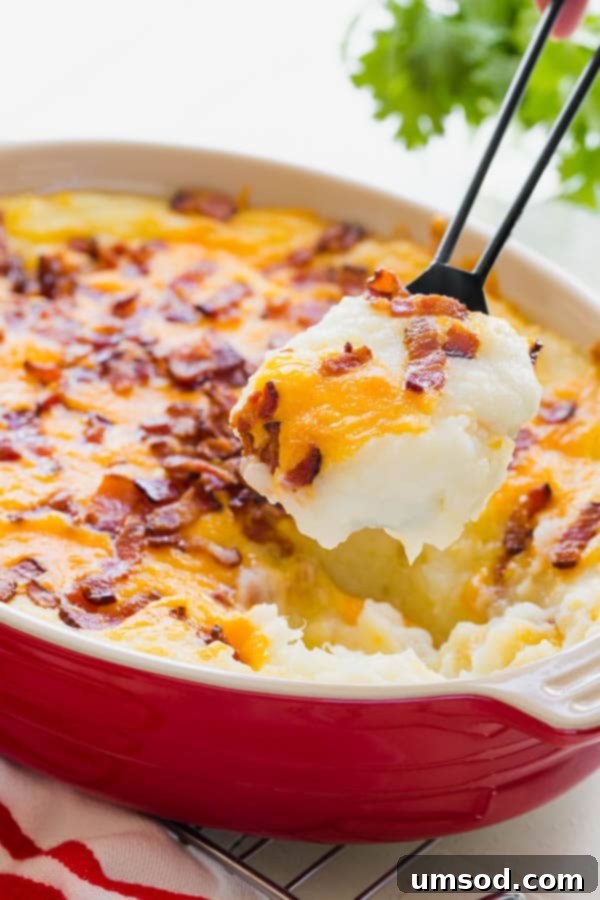 Ultimate Loaded Potato Bake 6 A serving spoon lifting a scoop of loaded mashed potato casserole from a baking dish, showcasing its cheesy, bacon-filled goodness.