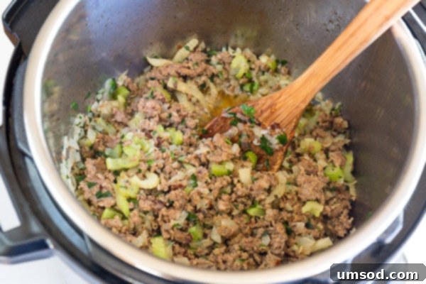 Sausage and finely chopped vegetables cooking together in an Instant Pot with a wooden spoon for stirring.