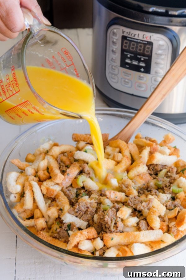 Egg and chicken stock mixture being poured over a bowl of sausage stuffing ingredients, ready for tossing.