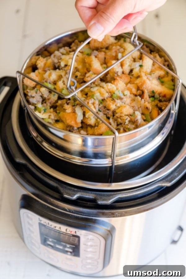 A cooked Instant Pot sausage stuffing pan being carefully lifted out of the Instant Pot using a handle.