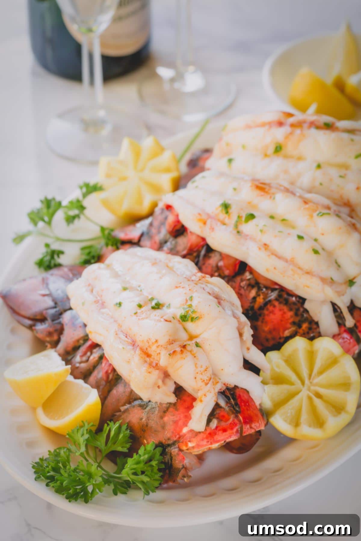 Cooked lobster tails on a large serving platter with cut lemon halves and fresh parsley.