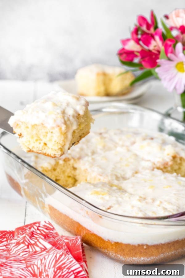 A slice of pineapple cake being lifted from a baking dish, showcasing its fluffy texture and generous frosting.