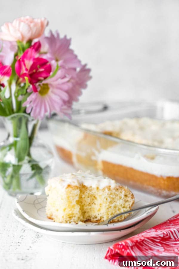 A perfectly sliced piece of pineapple cake on a white plate, with a fork having taken a bite, highlighting its moist interior and creamy frosting.