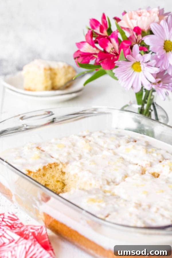 A baking dish filled with a beautifully frosted pineapple cake, with one square piece already removed, showing its tempting interior.
