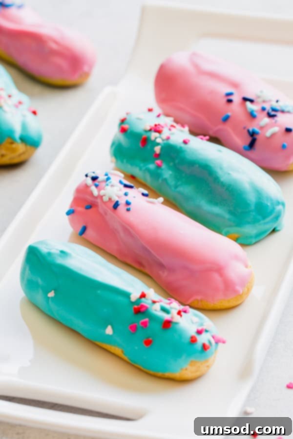 Pink or Blue Eclair Mystery 5 A close-up view of a stack of gender reveal eclairs with vibrant blue and pink frosting and sprinkles.