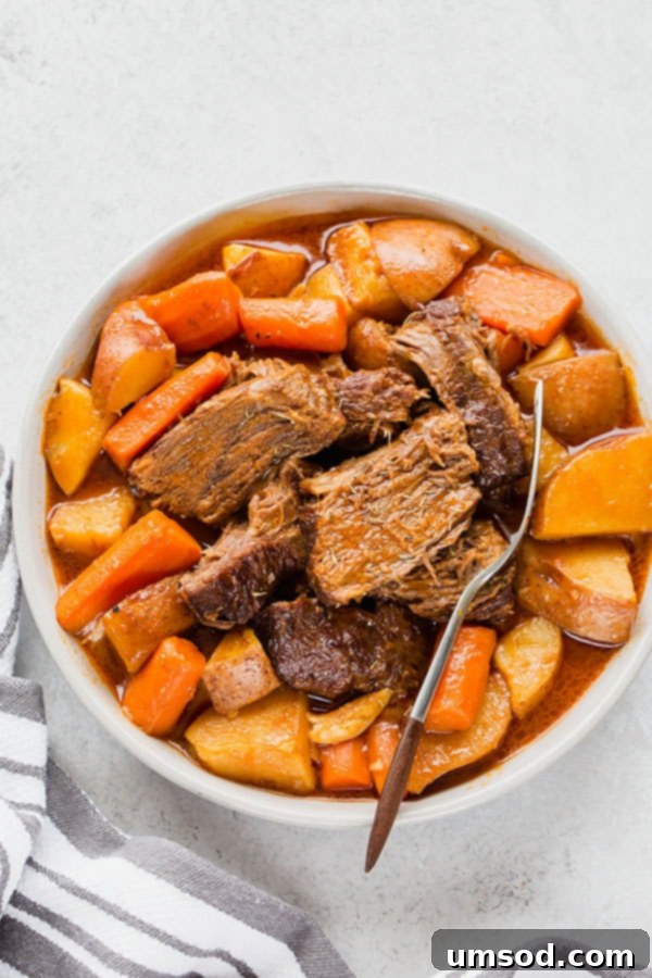 Plated pot roast with shredded beef, tender carrots, and potatoes, generously covered in rich, homemade gravy, served with crusty bread.