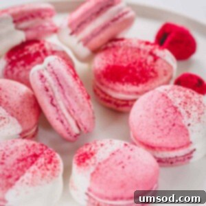 White chocolate dipped raspberry macarons arranged on a white platter.