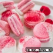 White chocolate dipped raspberry macarons arranged on a white platter.