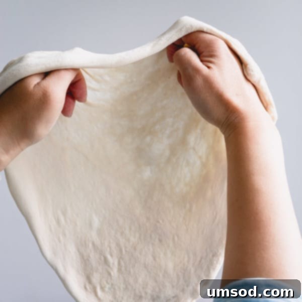 Effortless Homemade Pizza Dough 11 Close-up shot of two hands expertly stretching a pizza dough, demonstrating the technique.