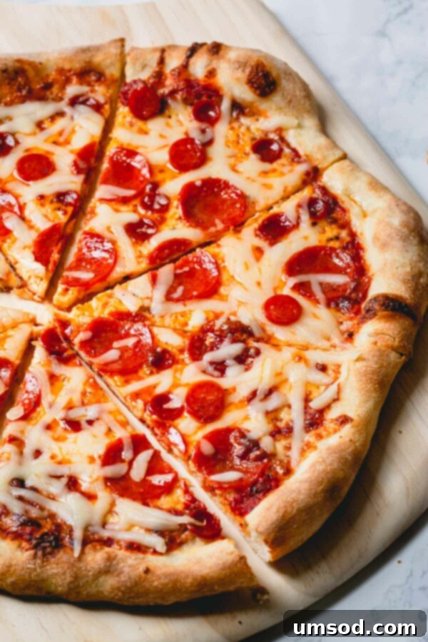 Effortless Homemade Pizza Dough 13 An overhead shot of a freshly baked, perfectly sliced pepperoni and cheese pizza on a rustic wooden board.
