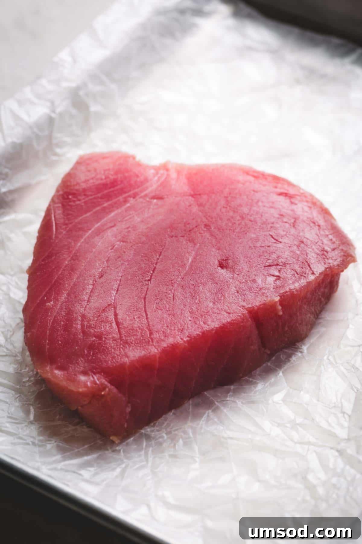 Sesame-Crusted Ahi Tuna 3 Raw ahi tuna steak on a white parchment paper.
