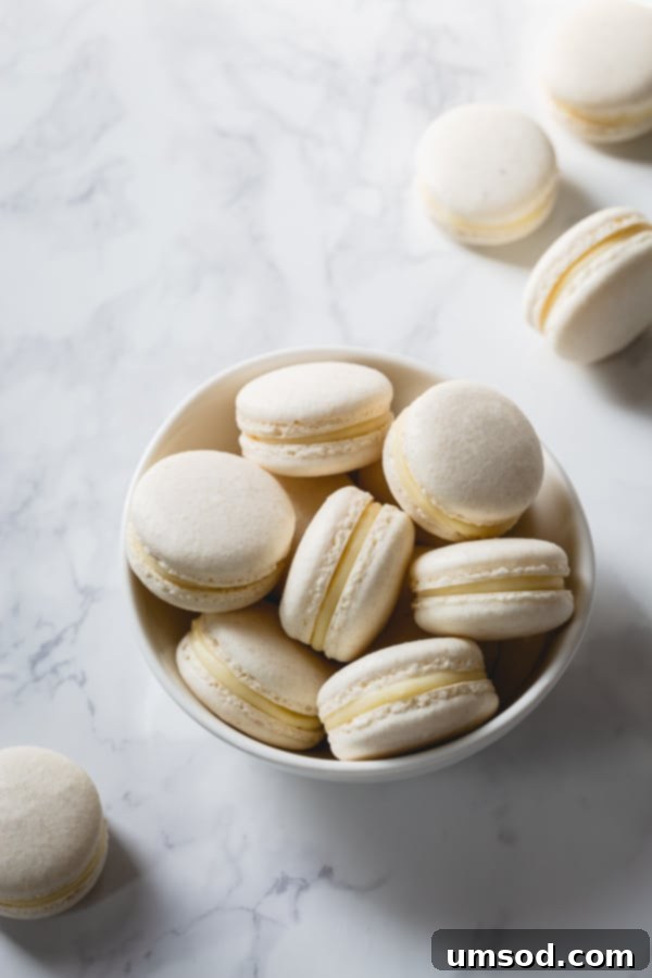 A pristine white bowl filled with beautifully assembled white macarons, each showcasing their smooth shells and creamy white chocolate ganache filling.