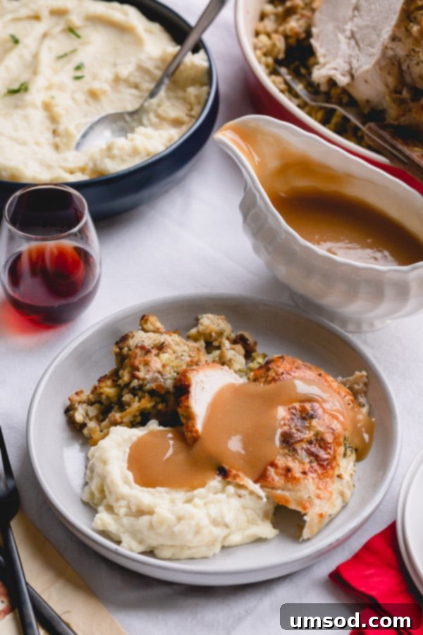 A plate of mashed potatoes, stuffing, and perfectly cooked turkey breast generously topped with rich turkey gravy. 