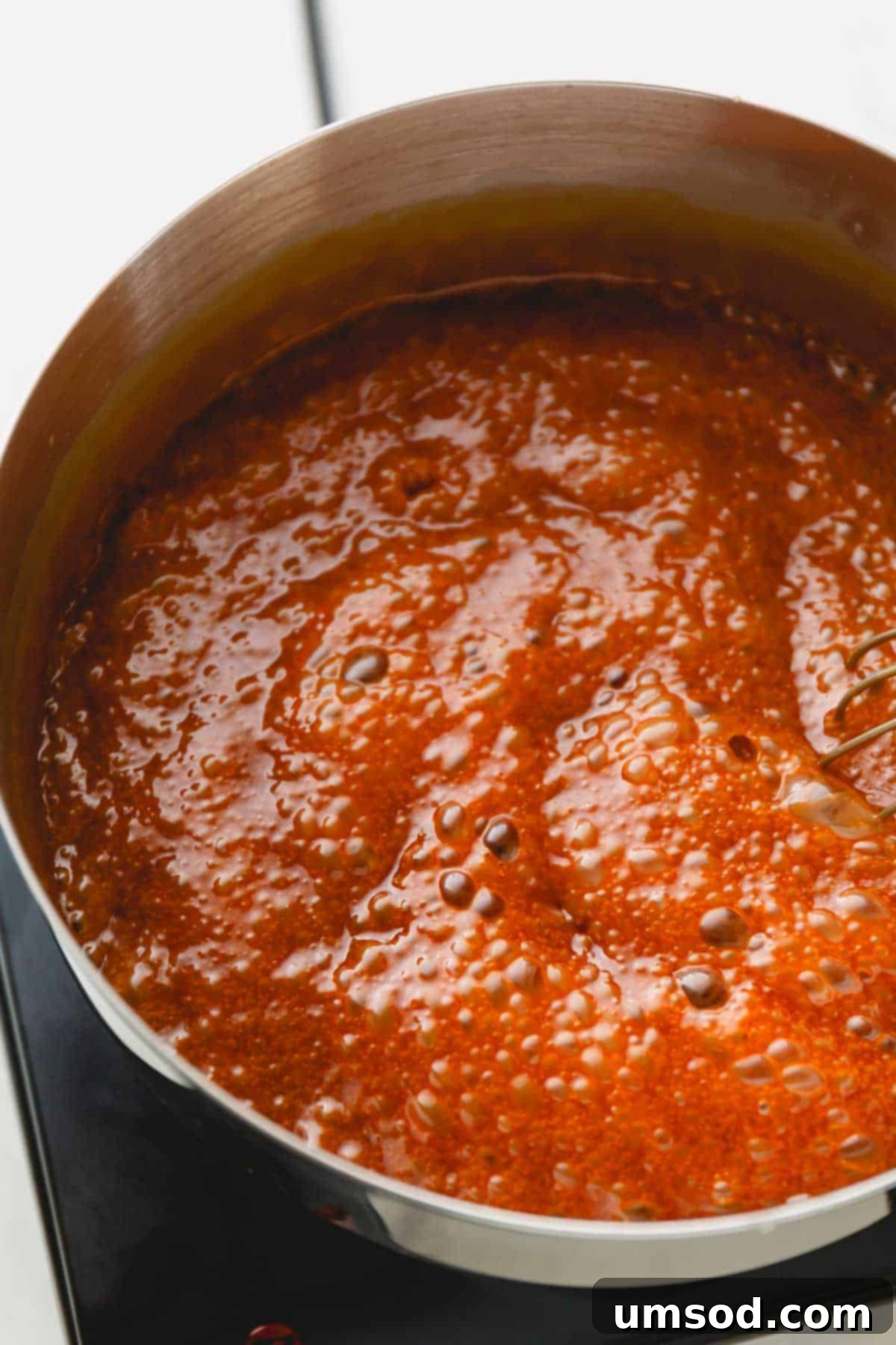 Homemade Caramel Sauce Dry Method Guide 3 Caramel sauce bubbling vigorously in a stainless steel saucepan, indicating the heating process.