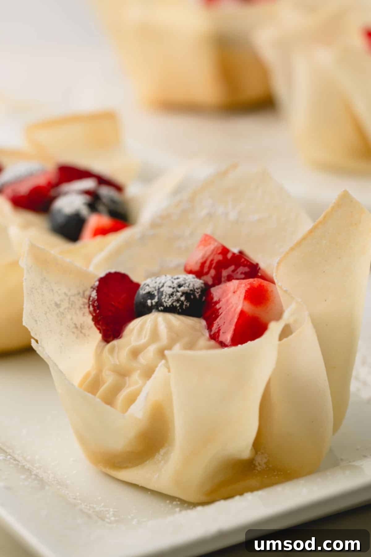 A single mini berry tartlet, showcasing its crisp spring roll wrapper crust and creamy berry topping.