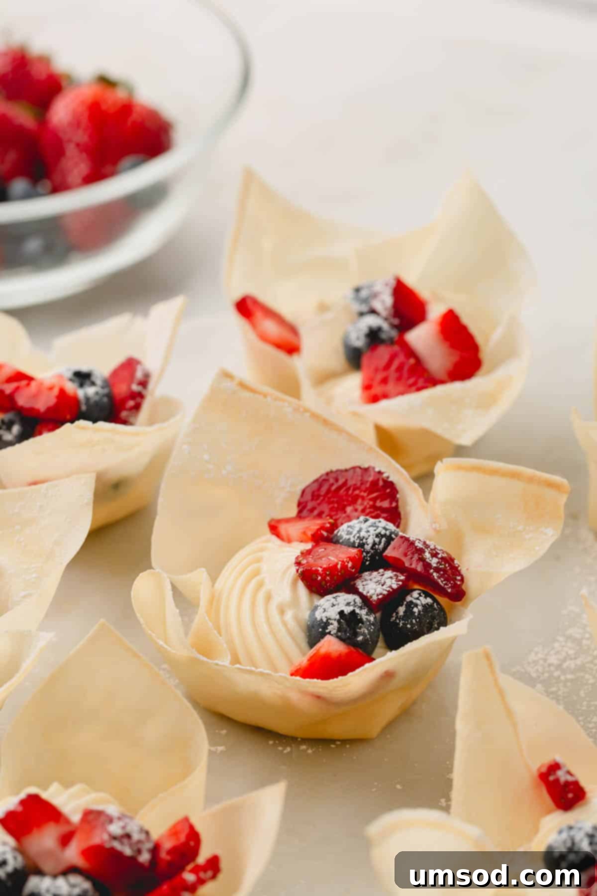 A close-up shot of several mini berry tartlets, beautifully adorned with fresh strawberries, blueberries, and a light dusting of powdered sugar.