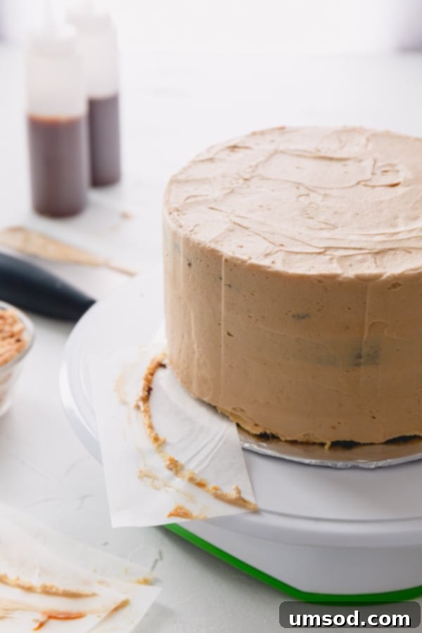 Chocolate Peanut Caramel Dream Cake 12 A crumb-coated cake with parchment paper being gently pulled from beneath, revealing a clean cake board.